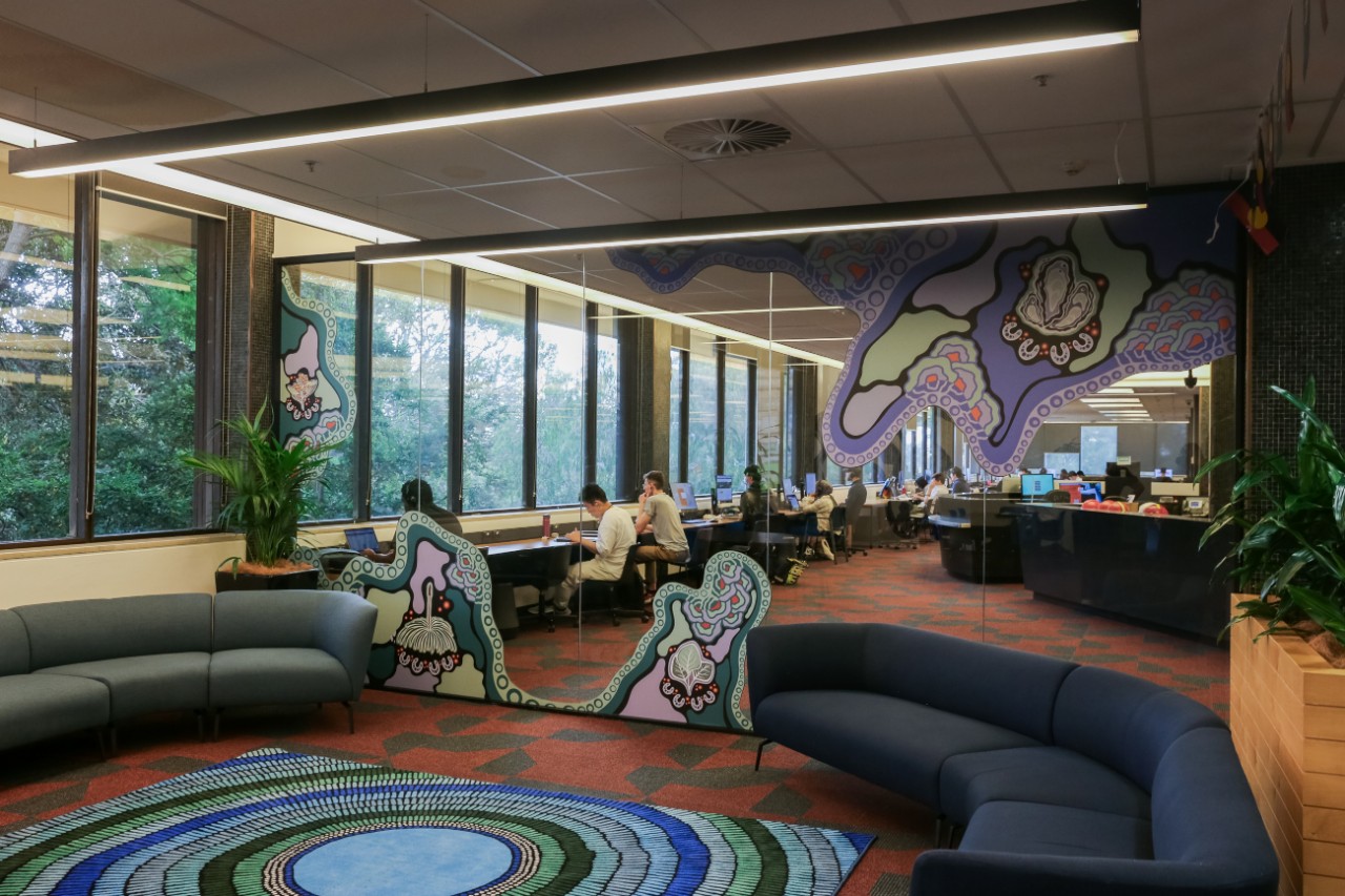 Aboriginal and Torres Strait Islander student space with blue couches and a glass wall featuring elements of Jessie Waratah's artwork Walking on Country.g