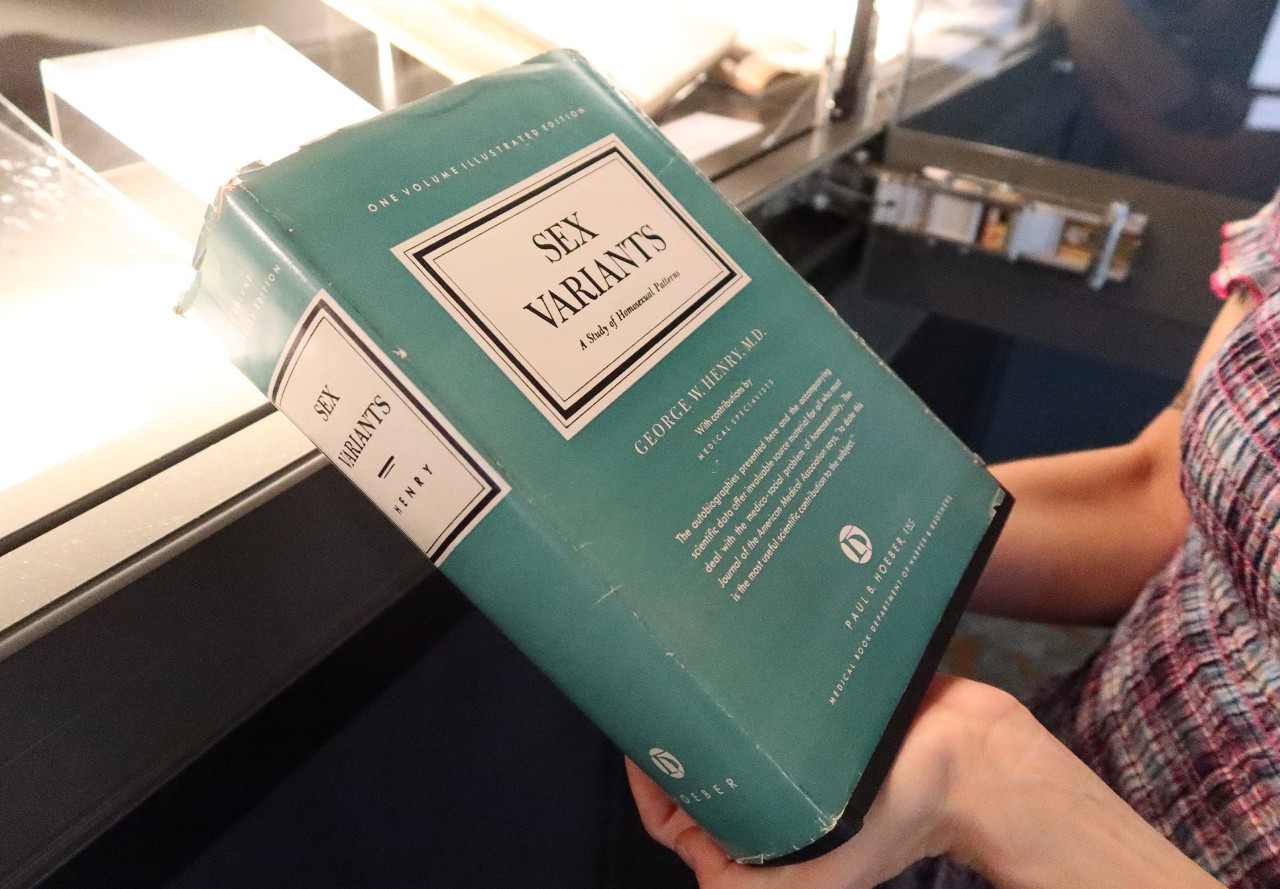 An angle shot of a pair of hands holding the book cover of 'Sex Variants' by George W. Henry. M.D