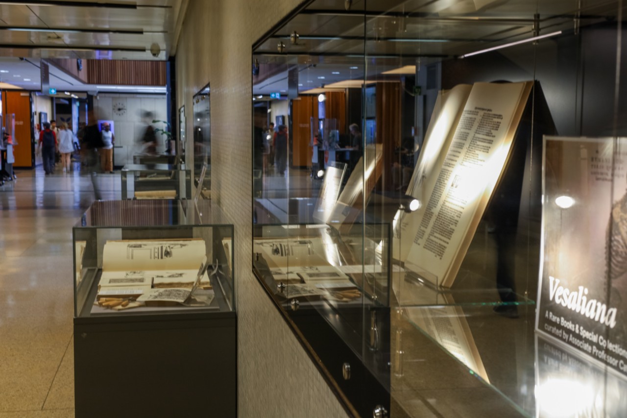 Glass display cases in Fisher Library with open books inside. 