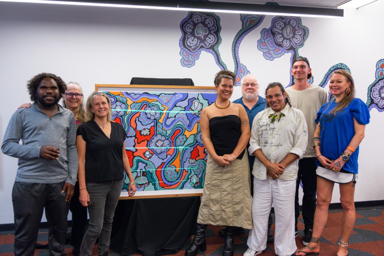 A group of people standing around the 'Walking on Country' artwork, smiling at the camera