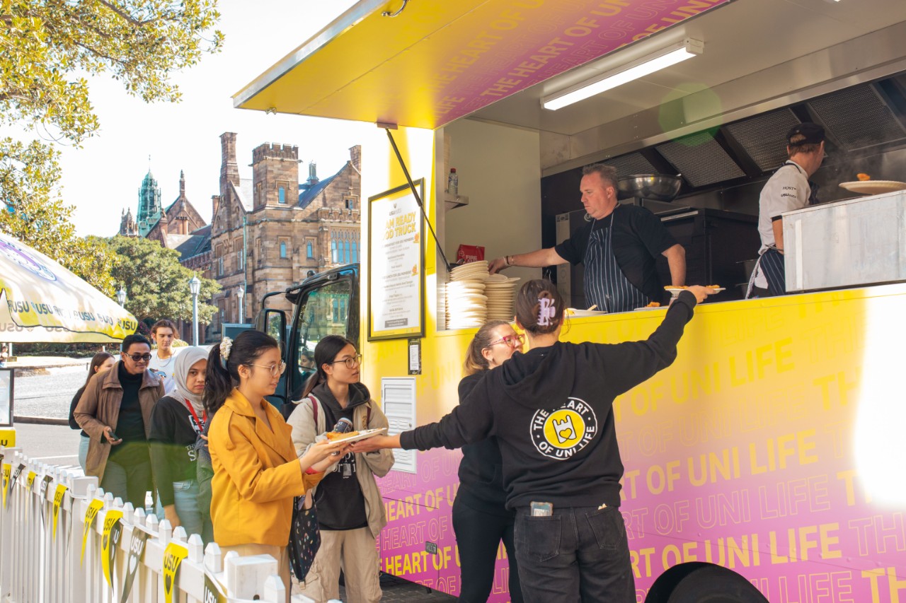 Image of a students lining up at a bright, yellow food truck on campus