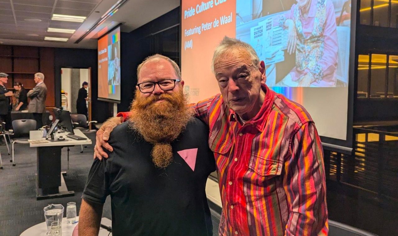 A photograph of two men with their arms around each other. On the left is Curt Flood, a man with a shaved head and red beard. On the right is Peter de Waal, an elderly man.